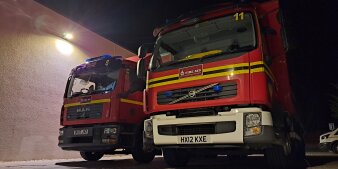 Zwei Feuerwehrfahrzeuge mit britischen Kennzeichen stehen im Dunkeln auf einem Parkplatz.