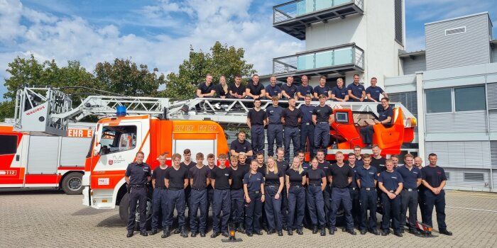 47 Männer und Frauen stehen vor und auf einem Feuerwehrfahrzeug. 