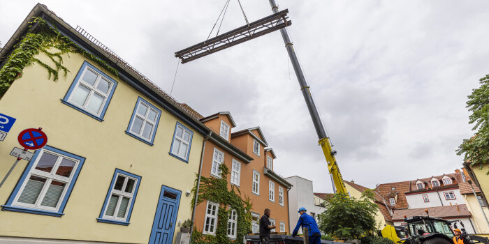 Foto: Aushub der Bergstrombrücke © Stadtverwaltung Erfurt Eine Brücke hängt an einem Kran und schwebt üver einem Haus.