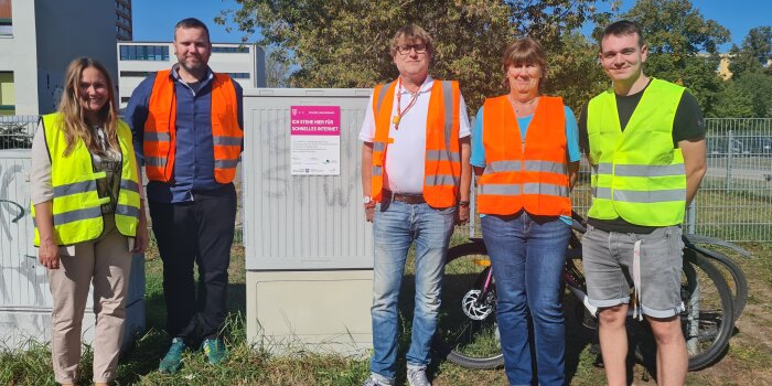 Ein Gruppenfoto von fünf Personen, die sich links und rechts neben einem Verteilerkasten aufgestellt haben. 