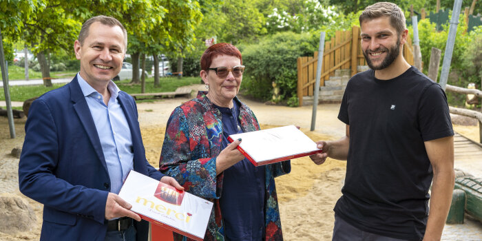 Ein Mann und eine Frau überreichen einem weiteren Mann zwei Pralinenschachteln. 