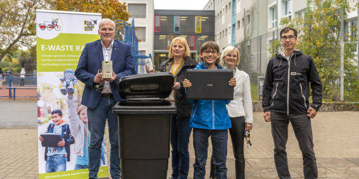 fünf Personen stehen an einer Mülltonne, ein Junge hält einen Laptop in der Hand