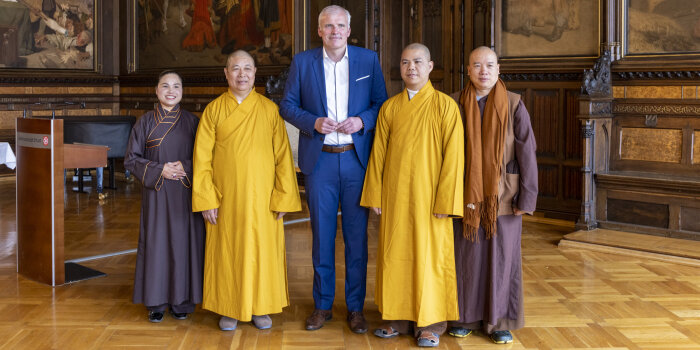 Ein Mann im Anzug sowie eine Frau und drei Männer in religiösen Roben stehen beisammen.