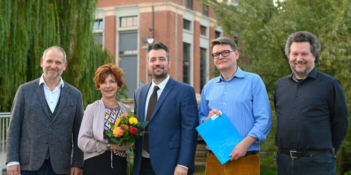 fünf Personen stehen nebeneinander, eine hält einen Blumenstrauß, eine eine Mappe