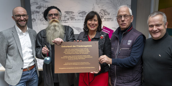 fünf Personen, drei von Ihnen halten eine Tafel mit Aufschrift "Geburtsort der Friedensgebete"