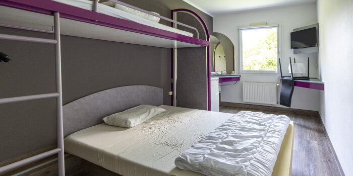 In einem Hotelzimmer steht ein einfaches Doppelbett. Im Überbau ist noch ein Einzelbett installiert.