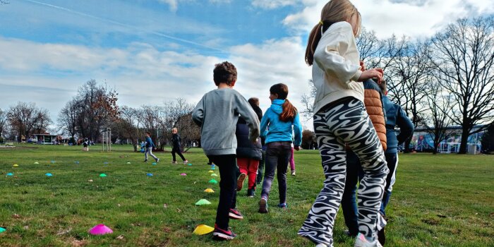 Rückansicht von Kindern, die auf einer Wiese einen Parcours aus bunten Hütchen meistern.