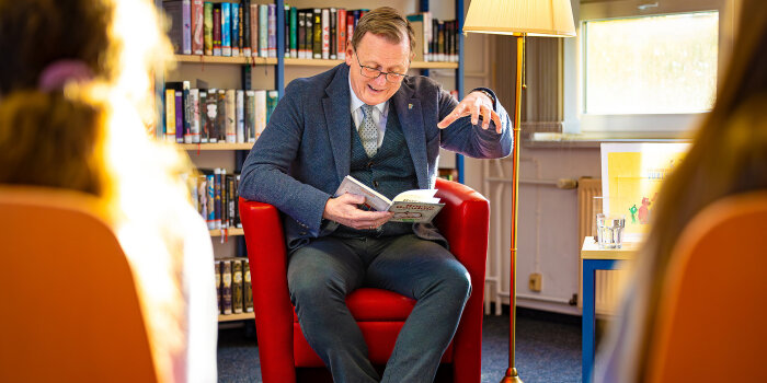 ein Mann sitzt auf einem roten Sessel und liest aus einem Buch