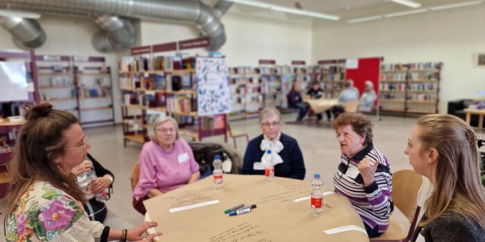 An einem Tisch sitzen sechs Frauen unterschiedlichen Alters und diskutieren miteinander. 