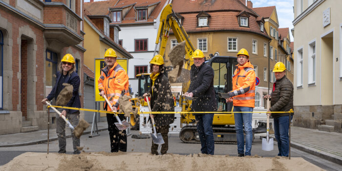 sechs Personen schippen Sand mit einer Schaufel