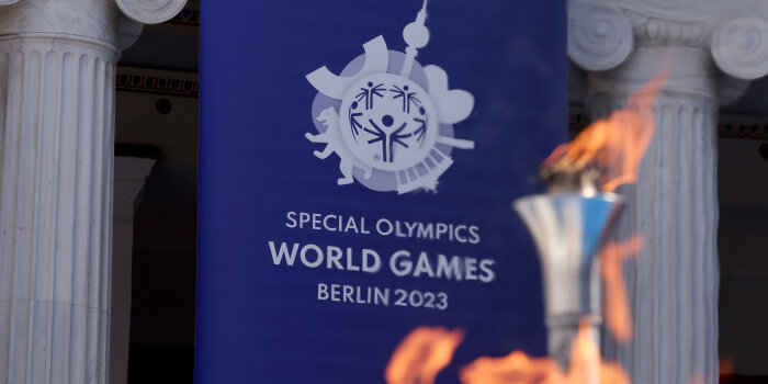 Vor einem Banner der Special Olympics 2023 brennt eine olympische Fackel.