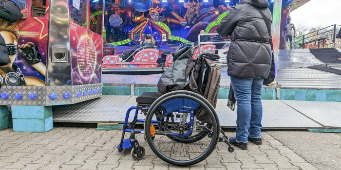 ein Rollstuhl steht vor einem Fahrgeschäft auf einem Rummel