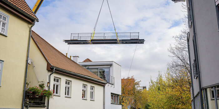 Foto: Einhub der Brücke in der Nonnengasse © Steve Bauerschmidt eine Brücke schwebt am Kran hängend über Häuserdächer