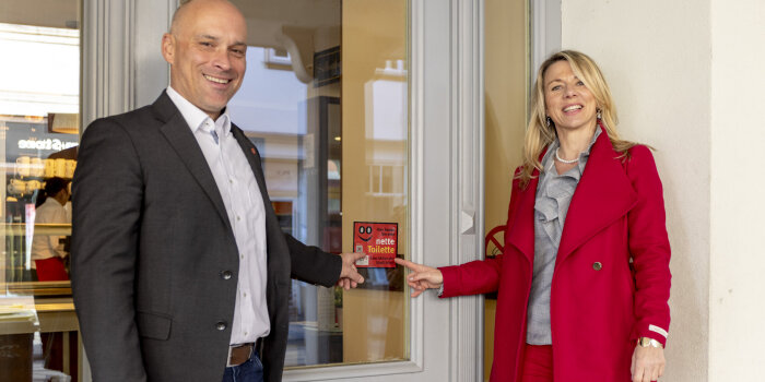 zwei Personen zeigen auf ein Schild mit Aufschrift "Nette Toilette"