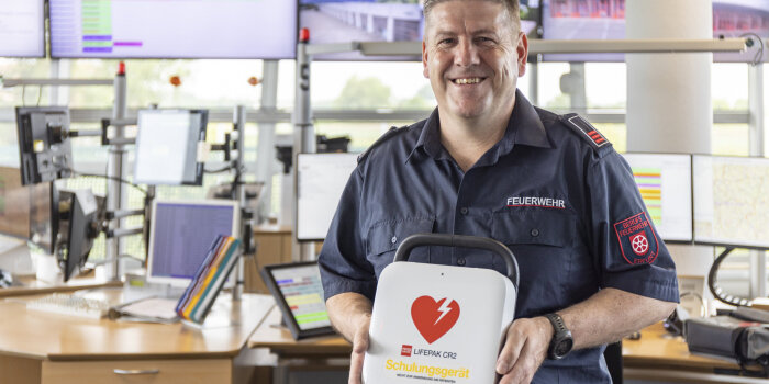 Ein Mann in Feuerwehruniform hält einen Defibrillator in der Hand.