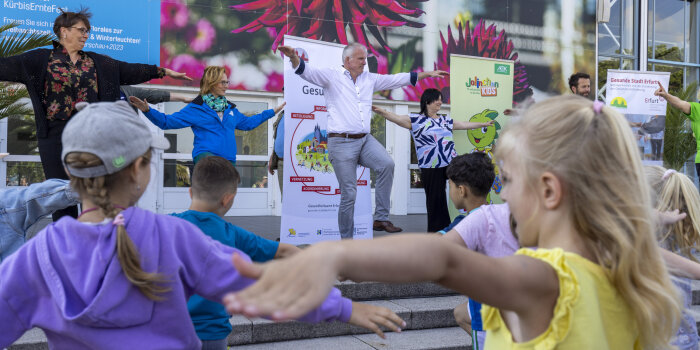 Viele Kinder bewegen sich vor einer Bühne, auf der Erwachsene vorturnen.