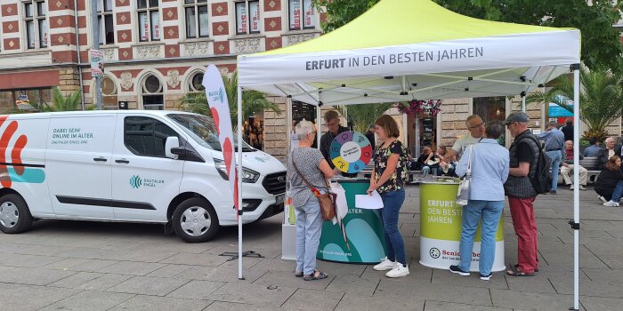 Auf einem Pavillon steht "Erfurt in den besten Jahren". Darunter sind sechs Menschen, die sich unterhalten.