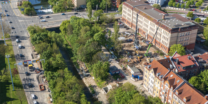 Luftaufnahme einer Baustelle zwischen einem Gebäude und einem Fluss