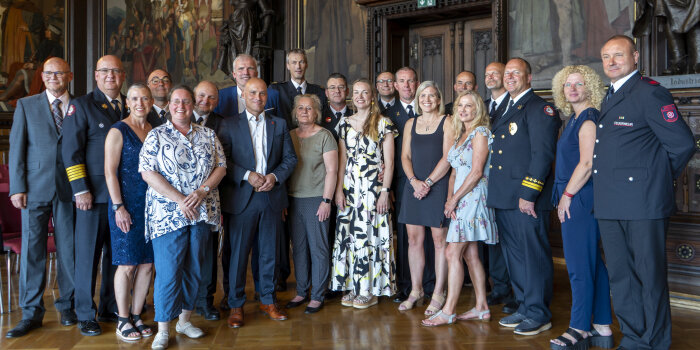 Eine Gruppe von Männern in Uniform und Anzug. Dazu Frauen in sommerlicher Kleidung.