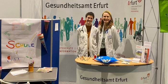 Zwei Frauen stehen an einem Messestand und warten auf Besucher.