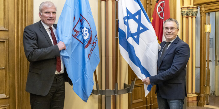 Zwei Männer posieren mit den Flaggen einer Stadt und eines Staates. 