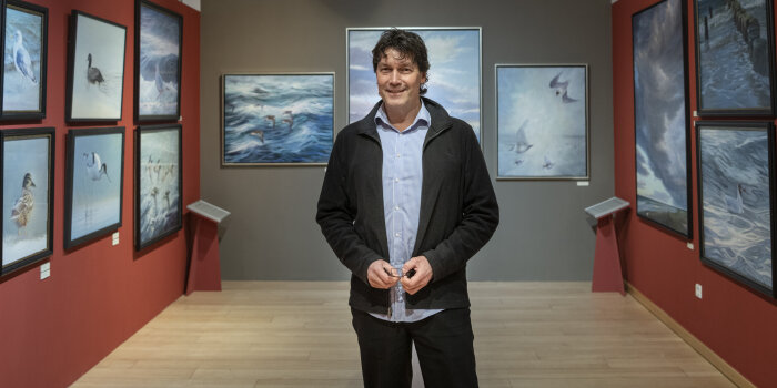 ein Mann steht in einem Ausstellungsraum, an den Wänden hängen Zeichnungen