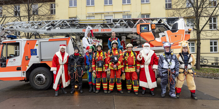 Menschen in Einsatzkleidung und Kostümen stehen vor einem Feuerwehrfahrzeug