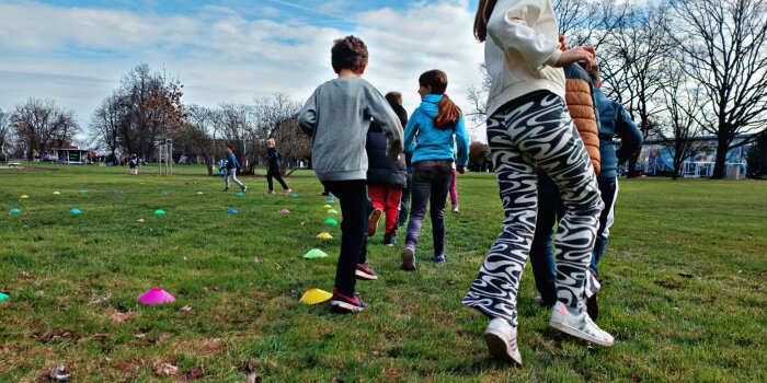 Rückansicht von Kindern, die auf einer Wiese einen Parcours aus bunten Hütchen meistern.