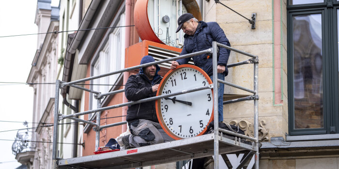 zwei Männer reparieren eine große Uhr
