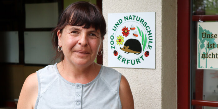 Eine Frau steht vor einem Schild mit der Aufschrift: Zoo- und Naturschule Erfurt.