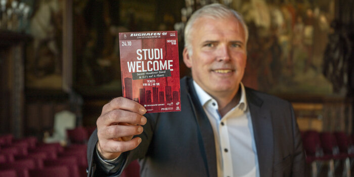 Ein Mann hält einen roten Flyer vor sich. Die Aufschrift: Studi Welcome.