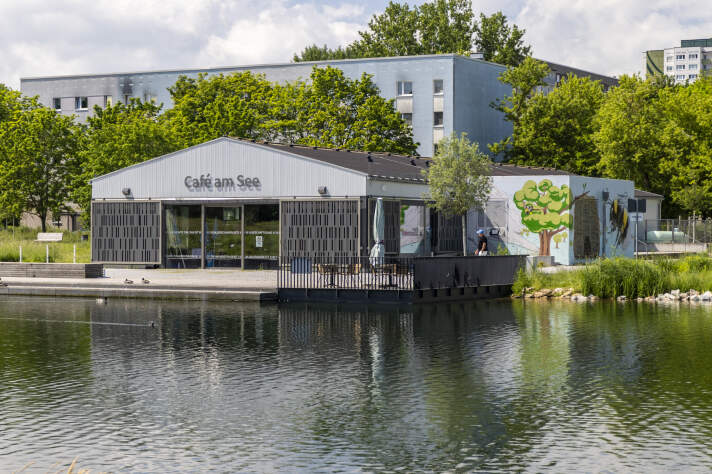 Ein Haus mit der Aufschrift „Café am See“. Davor ist der See zu sehen. 