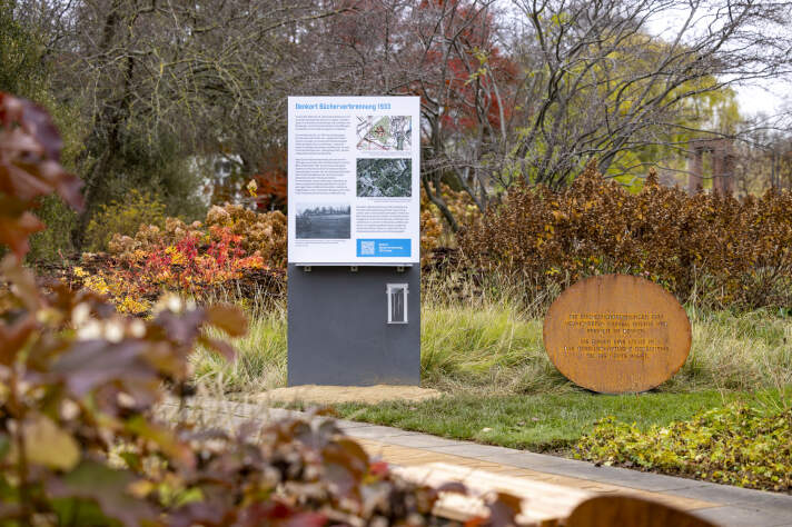 Informationstafel neben einem runden, rostfarbenen Metalldenkmal