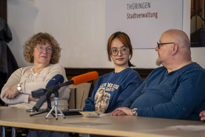 Drei Menschen sitzen nebeneinander an einem Tisch. 