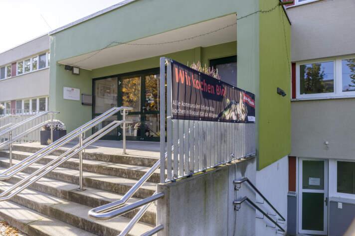 An einer Treppe in ein Gebäude hängt ein Plakat mit der Aufschrift: Wir kochen bio. 