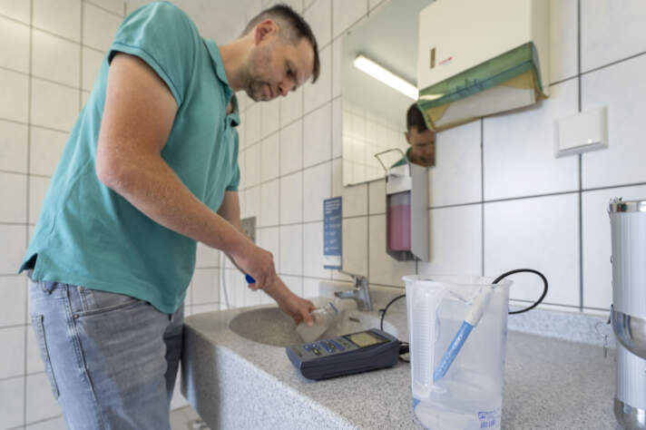 Ein Mann entnimmt eine Wasserprobe aus einem Wasserhahn. 