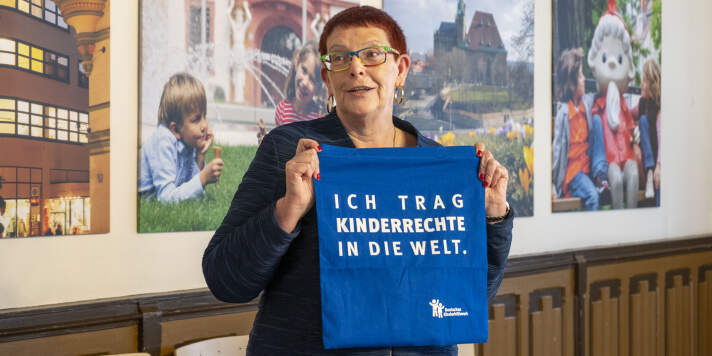 Eine Frau mit Brille und kurzen Haaren hält einen Beutel mit der Aufschrift: "Ich trag Kinderrechte in die Welt."