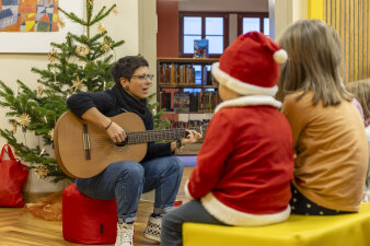 Eine Frau sitzt vor Kindern und spielt Gitarre.