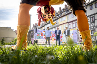 Till Eulenspiegel verbeugt sich, drei Männer stehen im Hintergrund