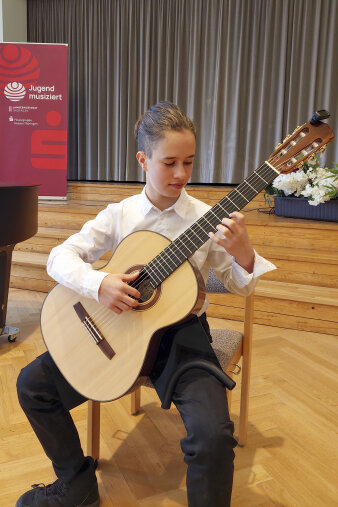 ein Junge in weißem Hemd und schwarzer Hose spielt Gitarre