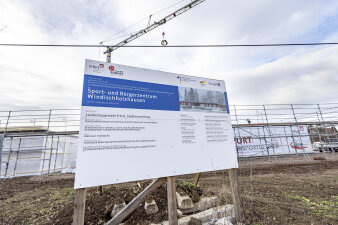 Ein Bauschild vor einem Rohbau