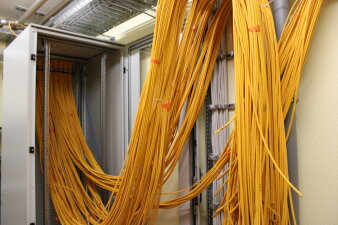 Viele gelbe Kabel hängen offen vor einem Schrank. 