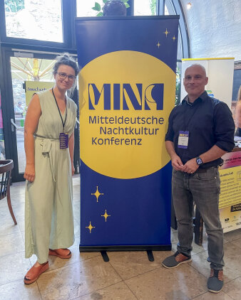 eine Frau und ein Mann stehen an einem Roll-up mit Aufschrift "Mitteldeutsche Nachtkulturkonferenz"