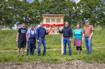 Personen stehen neben dem Insektenhotel und halten eine große Schleife in den Händen