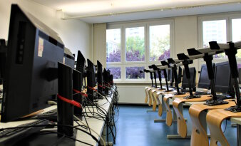 In einem Klassenzimmer stehen Computer und auf den Tischen sind Drehstühle hochgestellt.