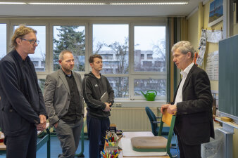 In einem Klassenzimmer stehen vier Männer und unterhalten sich.