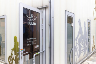 eine offenstehende Eingangstür mit Logo und Schriftzug "Nachteulen"
