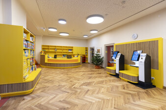 Der Empfangsbereich einer Bibliothek. Die Möbel sind in gelb und Holzoptik gehalten. 