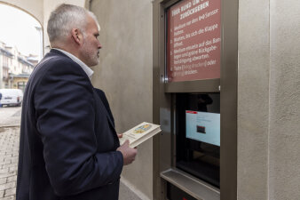 ein Mann steht an einem Automaten und hält ein Buch in der Hand