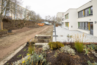 Eine Baustelle an einem sanierten Gebäude, davor ein Hochbeet